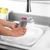 Hands washing a wine glass with a grey silicone dish brush in a white sink