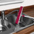 Pink floor brush with white handle being rinsed under tap in stainless steel kitchen sink