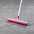 Pink and white rubber broom on grey carpet, shown cleaning pile.