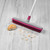 Pink and white rubber broom on grey carpet, shown cleaning pile.