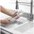 Pink handled dish brush cleaning a glass under running tap at kitchen sink
