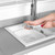 Hand washing a clear glass in a modern white kitchen sink.