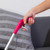 Pink handled grabber tool held by hand, shown above grey striped sofa cushions.