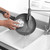 Person washing a grey non-stick frying pan under tap, scrubber cleaning surface