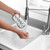 Washing a wine glass under running water with a grey and white cleaning pad