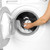 Hand placing laundry capsule in front load washing machine with towels