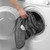 Hand placing grey electric heated blanket into washing machine
