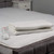 Folded white electric blanket with attached control on a grey upholstered bed