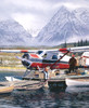 Close up of Last Chance wooden jigsaw puzzle presenting a lake by the snow-covered mountains where a plane is getting loaded with boxes of supplies, and a little boy fishes off the dock.