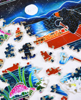  Pieces taken apart of Catching The Moon wooden jigsaw puzzle presenting a black bear paddling a red canoe around a lake with a fishing pole by its side. The moonlight glistens down on the water as it shines over the mountains. 