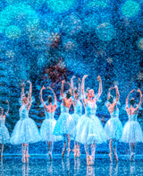  Close up of Snowflake Dance wooden jigsaw puzzle, displaying a group of ballerinas dancing on stage, all in the revelé position. Blue snowflakes fall all around the dancers. 