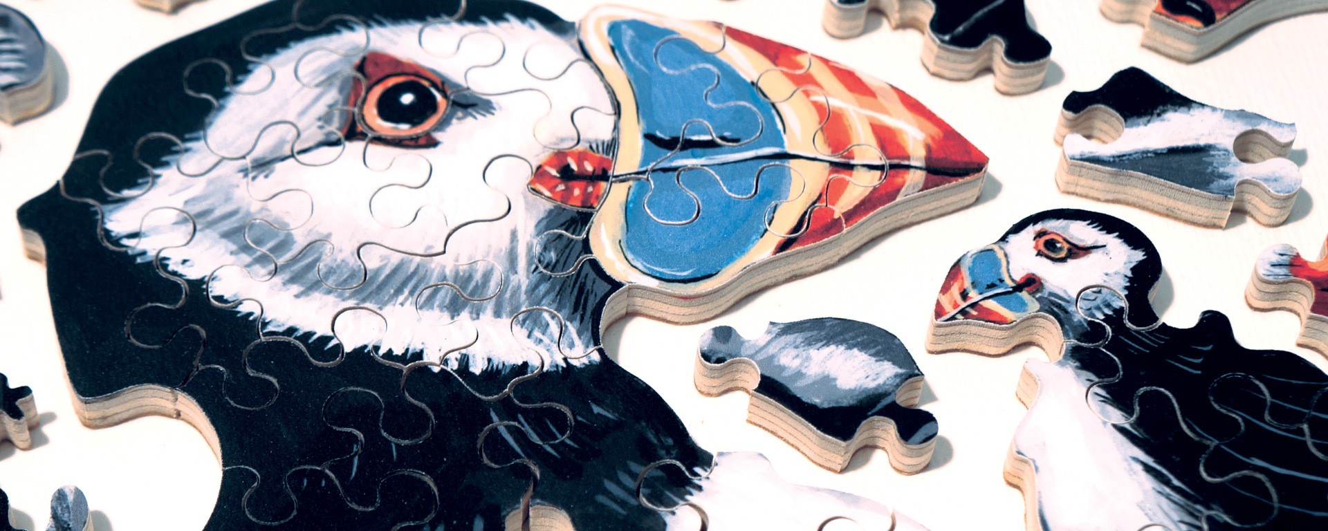 Wooden bird puzzle in progress featuring black and white puffins with red and blue beaks.