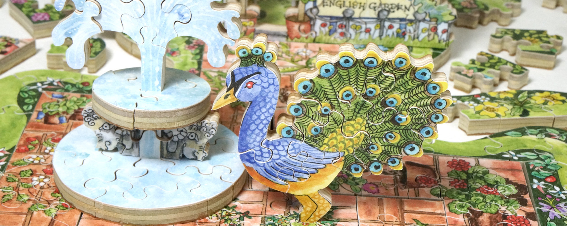 Wooden partially put together 3D puzzle of Cindy's English Garden showcasing a water fountain, peacock, and various colorful flowers and green plants.