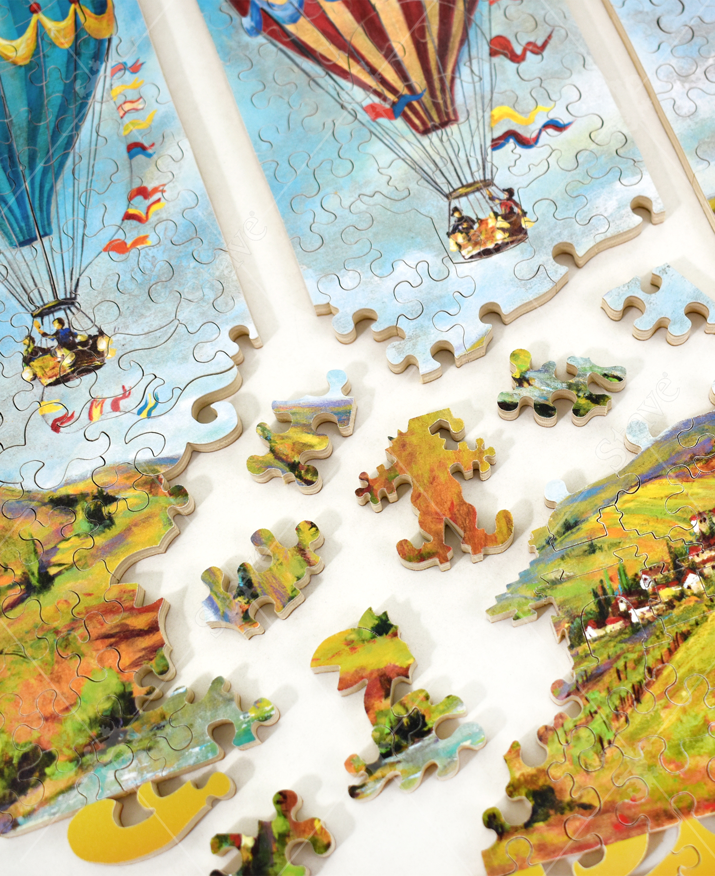 Pieces taken apart of Race Around The World wooden jigsaw puzzle showing two of the three panels, each capturing a hot air balloon soaring in the bright blue sky over a town located on a mountainous landscape.