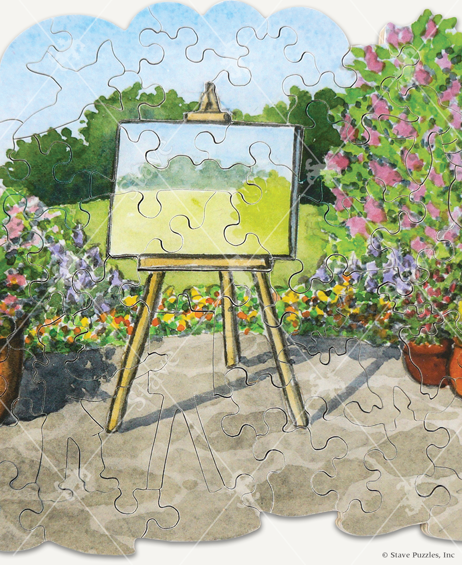 Close up of Picture This! wooden jigsaw puzzles displays an artist easel and canvas standing on a stone pathway surrounded by colorful flower bushes. The easel is facing a field with bushes in the background that are depicted in the painting on the canvas.