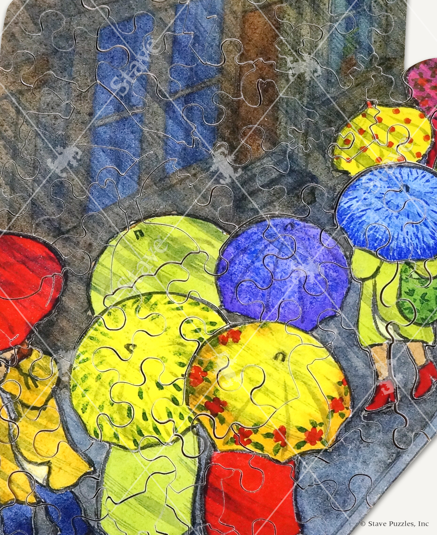 Close up of Let It Rain handcrafted wooden jigsaw puzzle displaying a rainy day in the city as people travel through the streets, carrying their bright umbrellas.