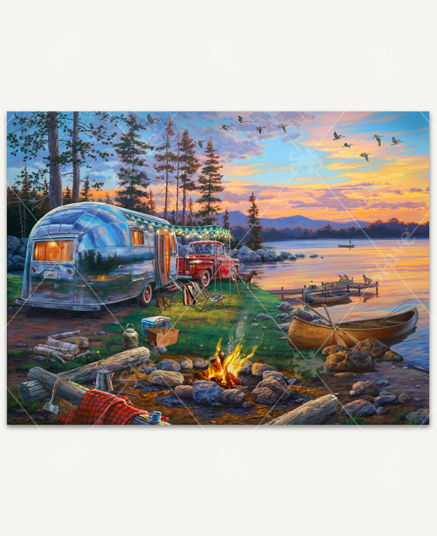 Happy Campers wooden jigsaw puzzle brings viewers to an evening scene of a campsite, where a vintage red pickup truck and Airstream camper are parked for the night. Log benches are layed in a horseshoe around a blazing fire. Two dogs look towards the lake as their owner is in a boat fishing. Geese fly overhead in the colorful sunset sky.