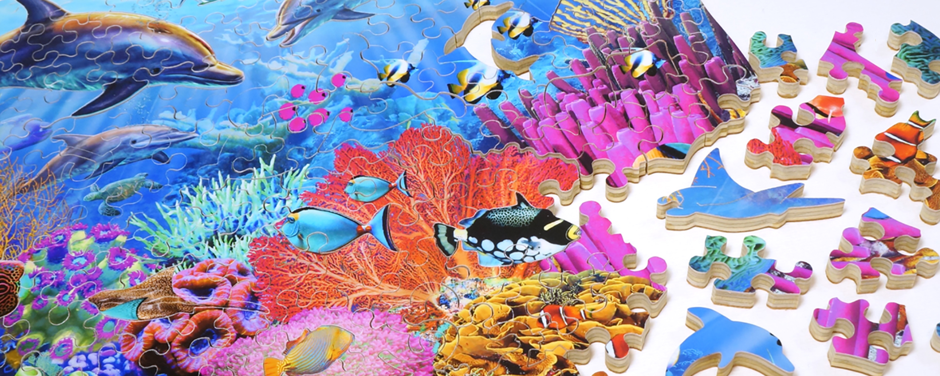 Wooden marine life jigsaw puzzle in progress featuring a colorful coral reef ocean scene with dolphins and fish as well as whimsy shaped puzzle pieces of dolphins and stingrays.