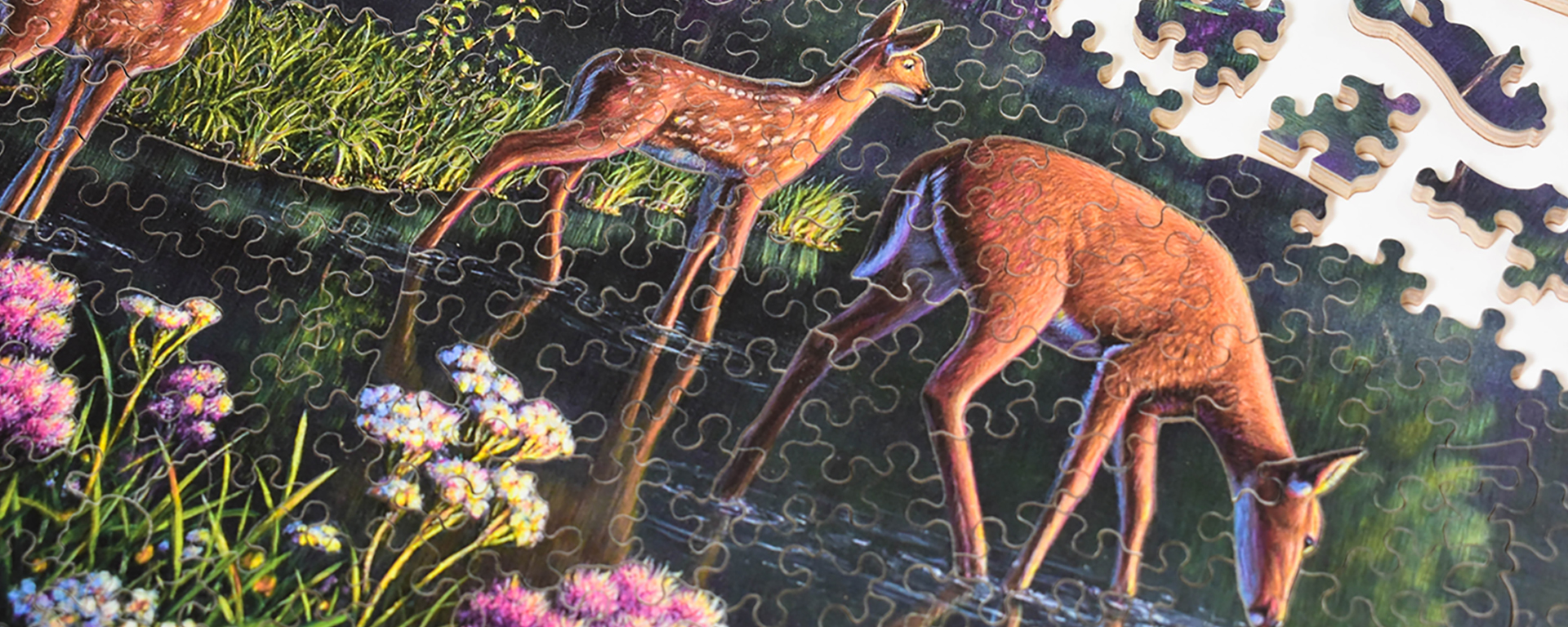 Wooden North American animal jigsaw puzzle in progress featuring a deer and her fawns taking a drink from a shallow pond.
