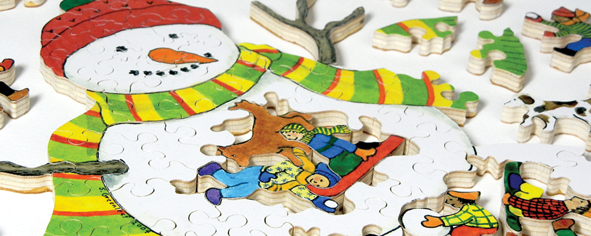 Wooden jigsaw snowman puzzle of children making a giant snoman and sledding in the snow.