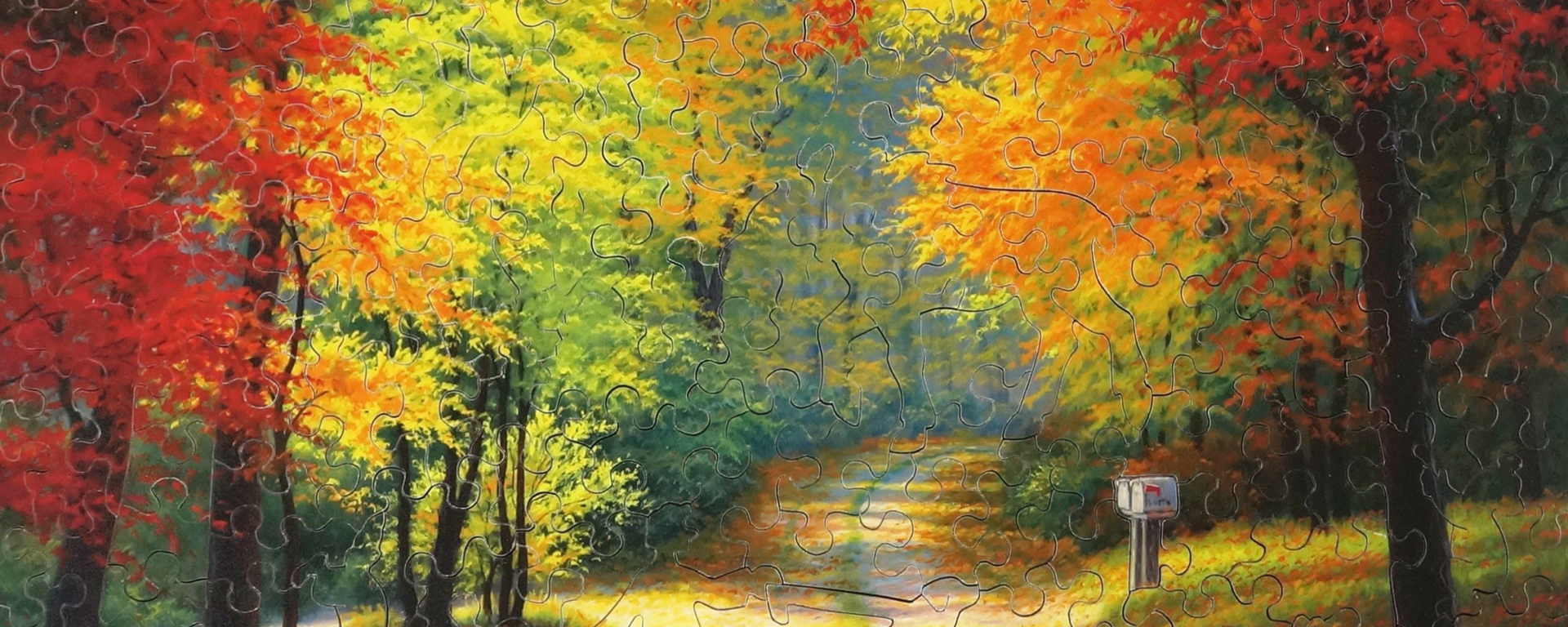 Wooden Autumn landscape puzzle depicting the changing of the leaves to vibrant reds, yellows, and oranges in autumn along a dirt road.