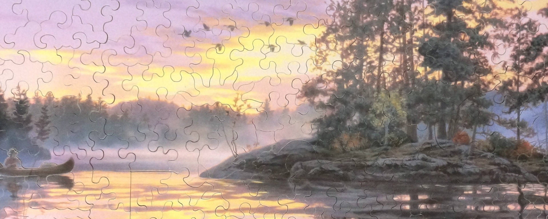 Wooden wilderness puzzle featuring a man paddling his canoe towards a small island on a misty lake.