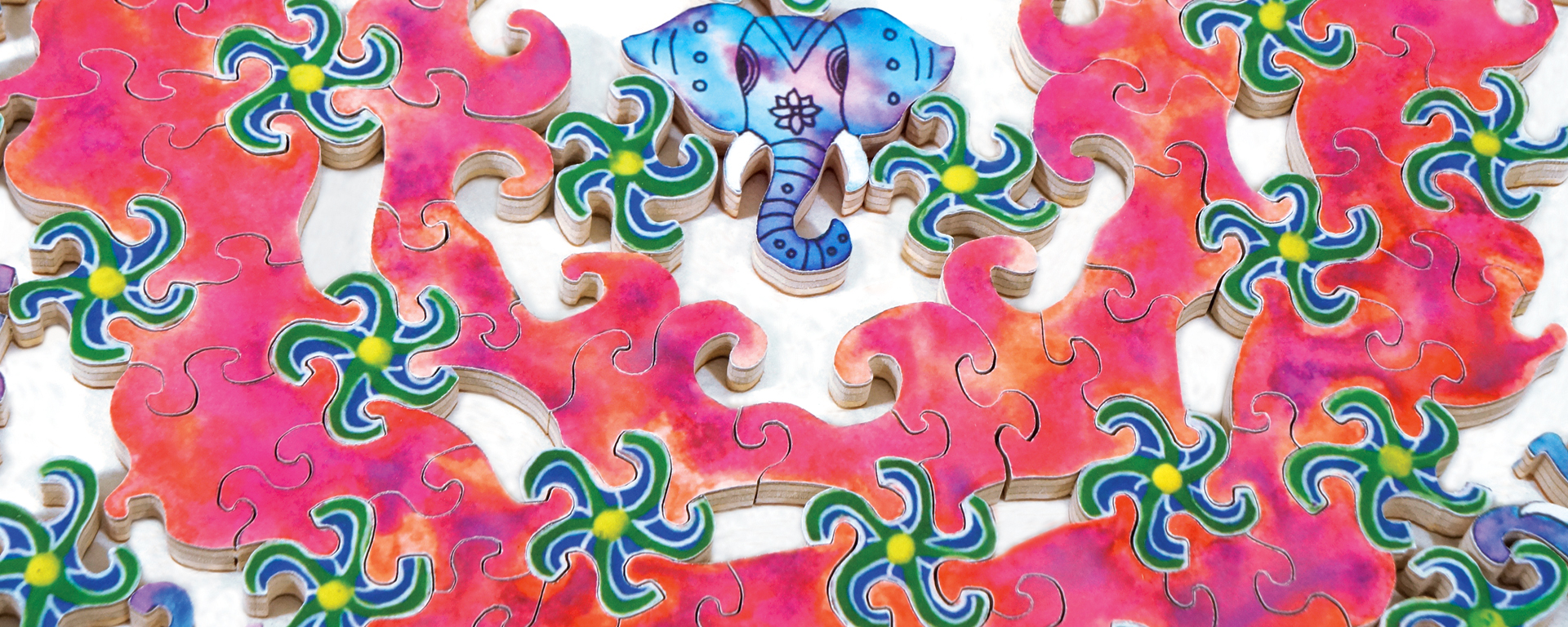 Wooden mandala puzzle featuring an elephant and green/blue swirls all surrounded by a hot pink background.
