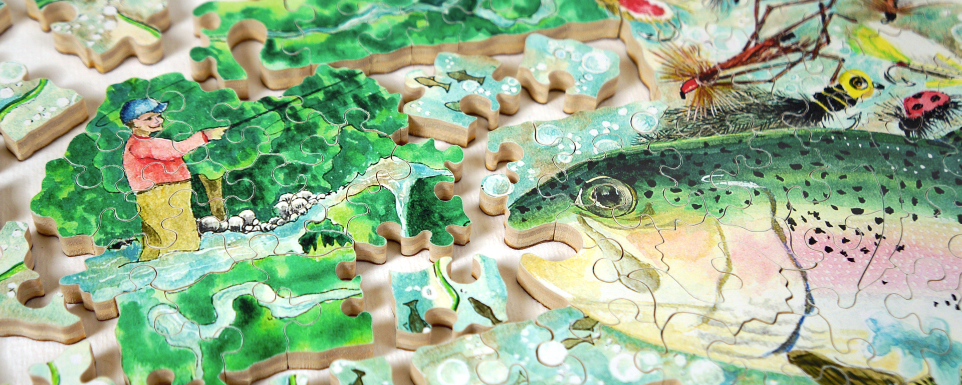 Wooden fishing puzzle in progress featuring a man fishing in a stream with a large rainbow trout in the foreground.