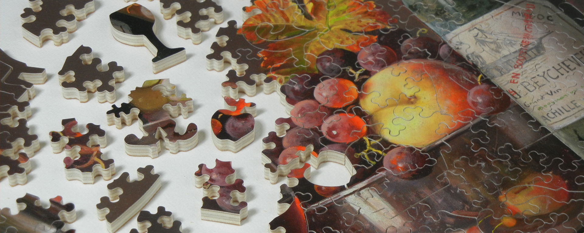 Wooden still life puzzle in progress featuring a fruit bowl and whimsy shaped pieces such as an apple, wine glass, and the Stave logo.