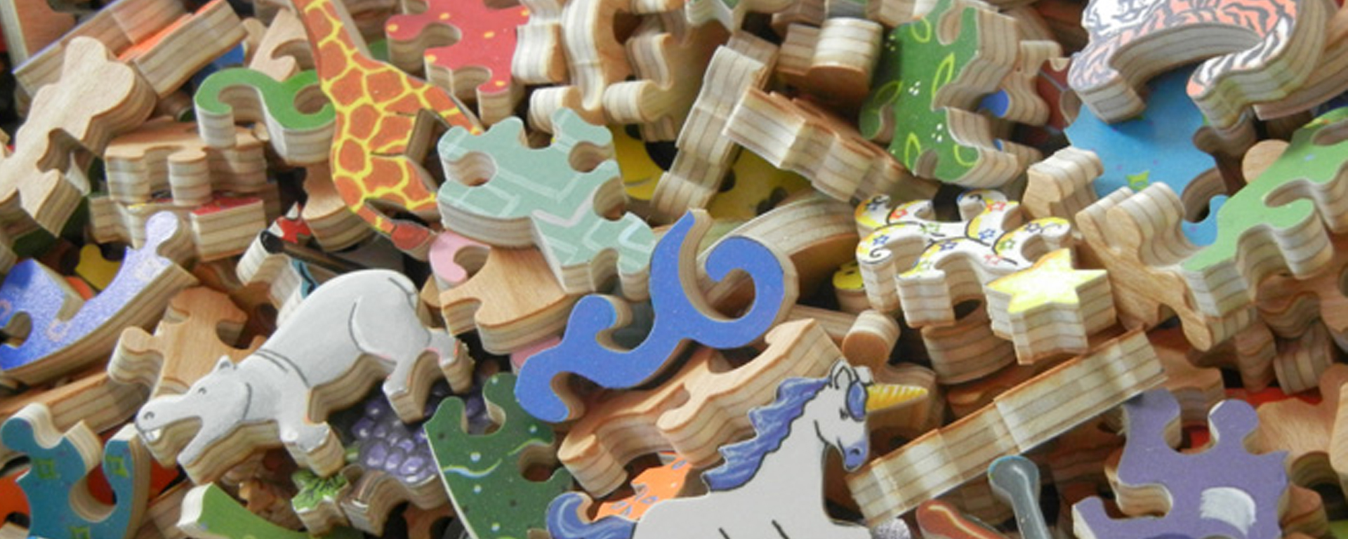 Wooden alphabet puzzle pieces piled on top of each other. The puzzle features whimsy shaped pieces such as a unicorn, giraffe, hipppo, and other various brightly colored pieces.