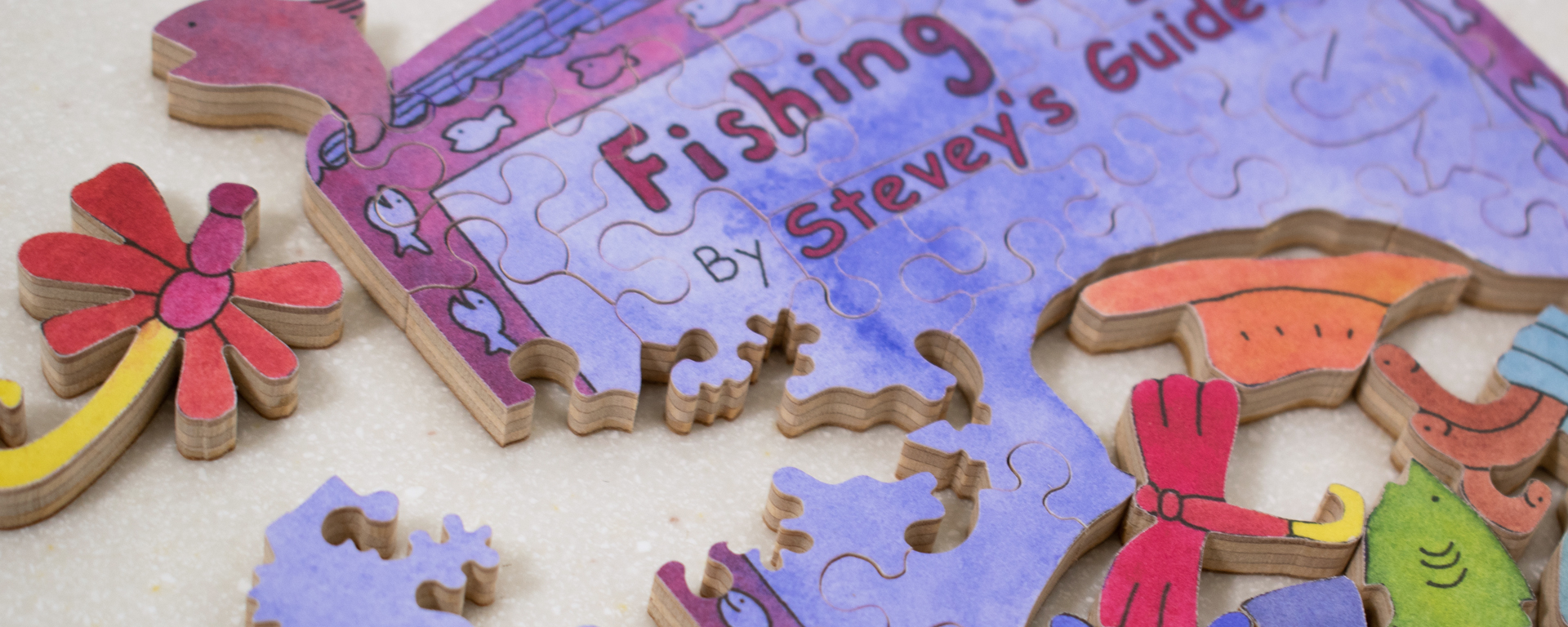 Wooden book shaped puzzle in progress of a purple and pink fishing book. The book has the author, as well as fish, dragonflies, and worms featured on it.