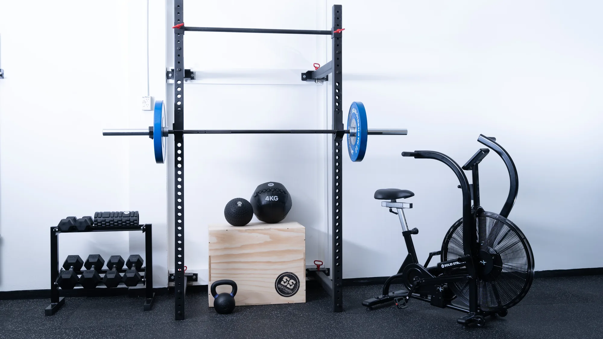 A Solid Strength home gym package: rack, barbell, plates, dumbbells, kettlebells, plyo box and air bike