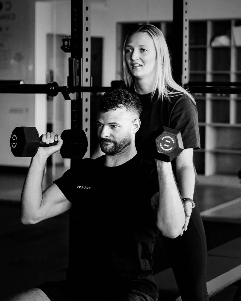 A coach guiding a client through a dumbbell press at The Cove Wellness