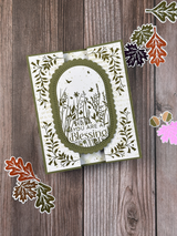Handmade greeting card featuring an oval botanical frame with intricate olive green foliage, gold foiled accents, and a delicate floral design.