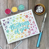 Handmade greeting card with colorful snowflakes and thinking of you sentiment with crafting materials in background.