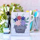 Handmade greeting card with flowers in a pail with hello sentiment on it and crafting materials in background.