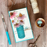 Handmade greeting card with flowers in a vase and happy birthday sentiment on it with crafting materials in background.