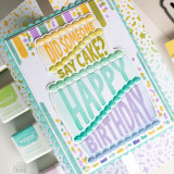Handmade greeting card with layered cake on it with did someone say cake? happy birthday sentiment on int with crafting supplies in the background.