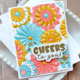 Handmade greeting card with paper fans on it and cheers to you sentiment on it with cardstock in background.