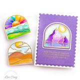 A handmade card with mountain reflection inside arched window frame with two window frames laying next to the card of a sunrise and rolling hills.