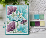 Handmade greeting card with flowers on it and happy birthday sentiment on it with crafting materials in background.