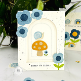Handmade greeting card with mushrooms, flowers, and a snail with sorry I'm slow... sentiment on it with flowers and snails in the background.