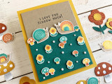 Handmade greeting card with mushrooms, flowers, and snails on it with I love you slow much sentiment with mushrooms, flowers, and snails in the background.