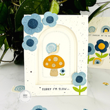 Handmade greeting card with mushrooms, flowers, and a snail with sorry I'm slow... sentiment on it with flowers and snails in the background.