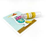 Container of small cube embellishments resembling ice cubes for paper crafting, shown on a handmade greeting card featuring a colorful drink illustration.