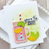 Handmade greeting card with a drink cup, citrus fruit, and you're the zest sentiment on it with cardstock in the background.