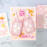 Handmade greeting card with two drink cups and clink, laugh, and repeat and cheers to you sentiments on it with cards in background.