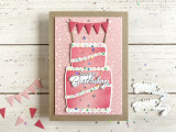 Handmade greeting card of layered cake with confetti and happy birthday sentiment on it with crafting materials in the background.