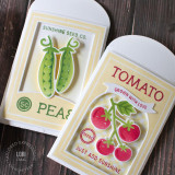 Two handmade greeting card gift holders, one with tomatoes on it and grown with love sentiment and the other with two peas on it with card in the background.
