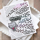Handmade greeting card with foiled heart rays on it with cat holding heart and delivering loads of love sentiment on it with cardstock in background.